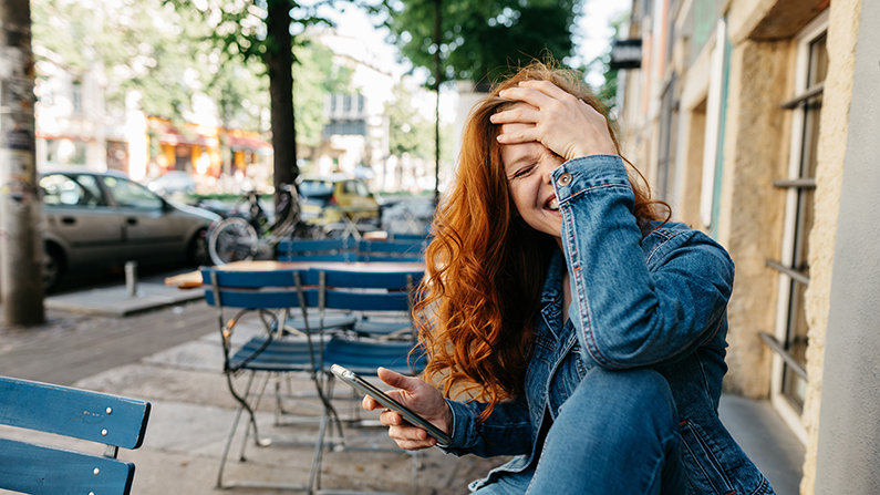 Lachend persoon op een terras, met een smartphone in de hand